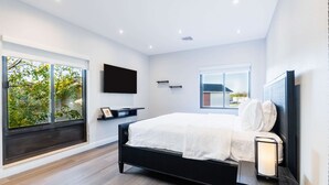 A modern bedroom with a large bed, a TV mounted on the wall, and a window with a view of greenery. - Hampton Inn & Suites Fairfield (Fairfield)