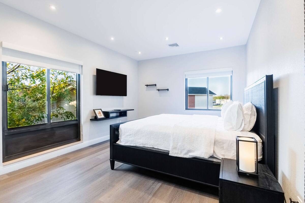 Quarto moderno com uma cama grande, televisão na parede e janela com vista para áreas verdes.