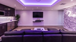 A modern living room with a sectional sofa, a flat-screen TV mounted on the wall, and a decorative wall with a number '2' design. - Hampton Inn & Suites Fairfield (Fairfield)