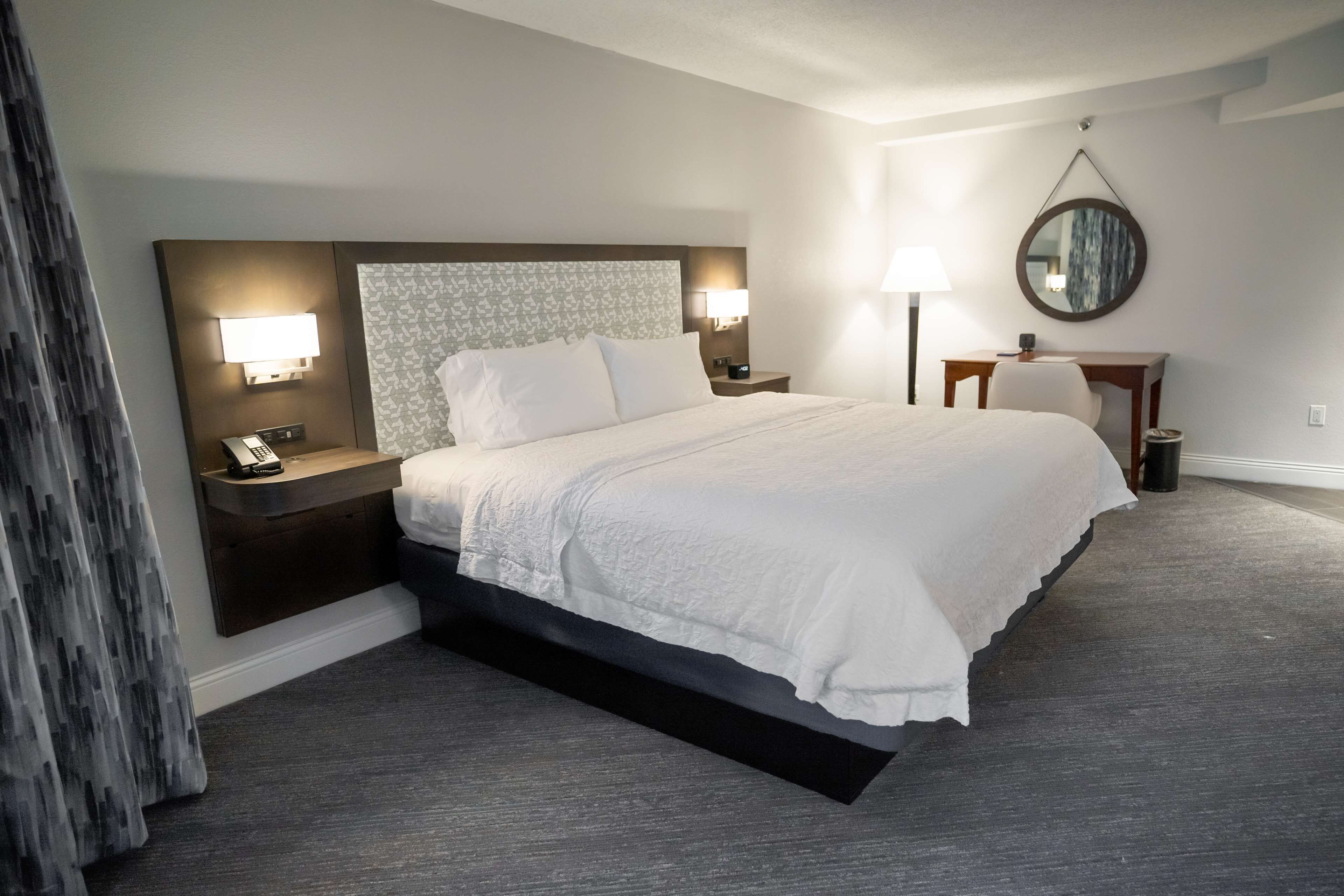 A hotel room with a large bed, bedside lamps, a desk, and a mirror on the wall.