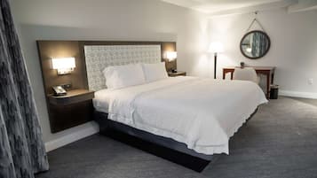 A hotel room with a large bed, bedside lamps, a desk, and a mirror on the wall.