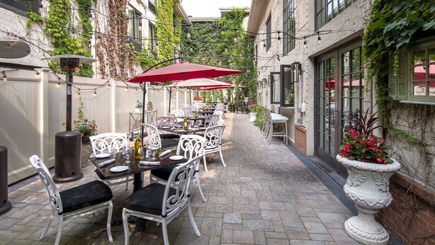 An outdoor patio with white metal chairs and tables, red umbrellas, and potted plants. - Hampton Inn & Suites Fairfield (Fairfield)