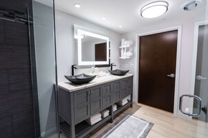 Un baño moderno con un espejo grande, dos lavamanos, una puerta de madera oscura y un box de ducha de vidrio.