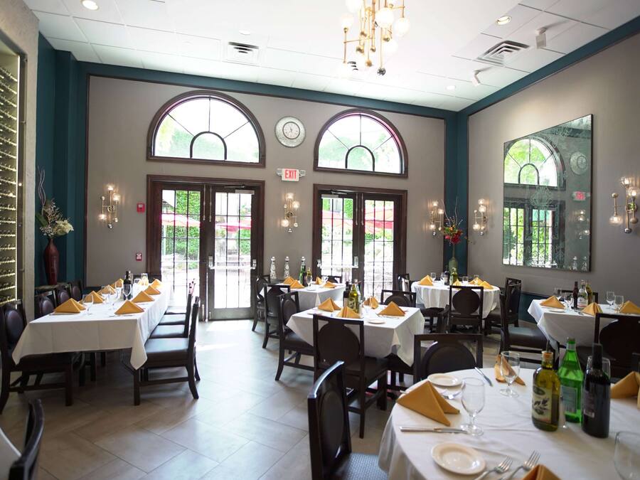 A restaurant with multiple tables, each set with white tablecloths, yellow napkins, and wine bottles.