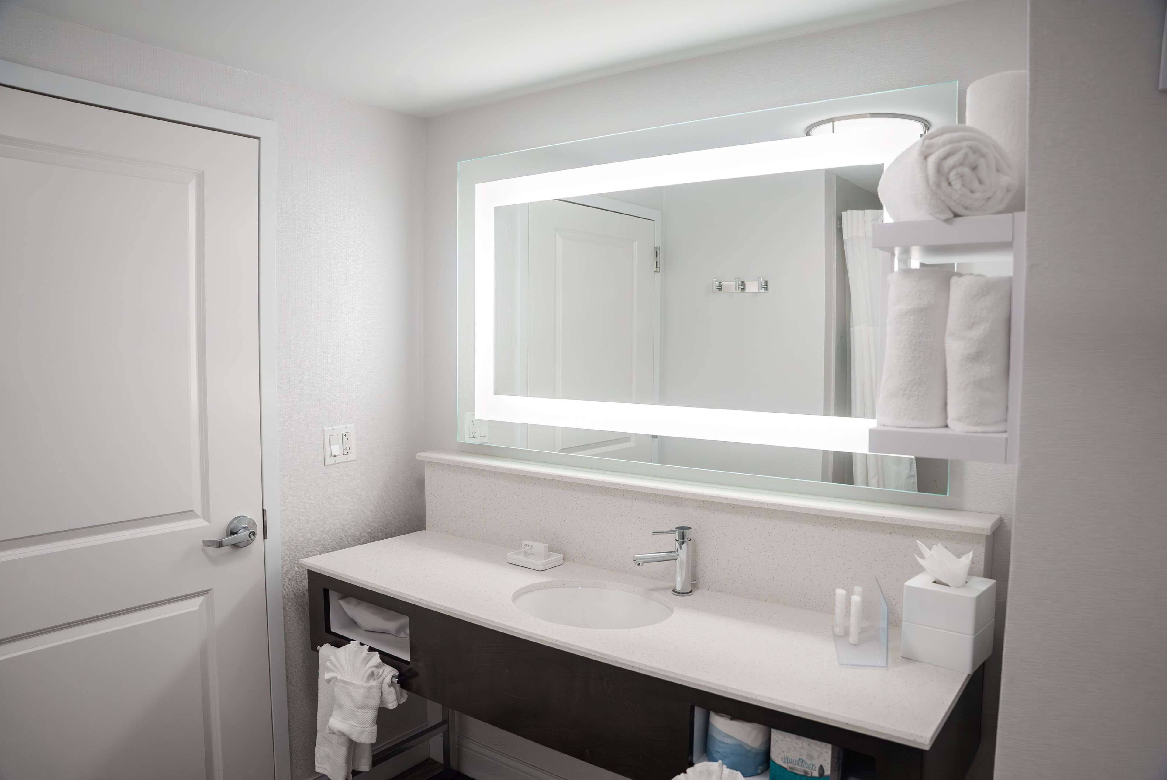 A modern bathroom with a white sink, a large mirror, and a towel rack.