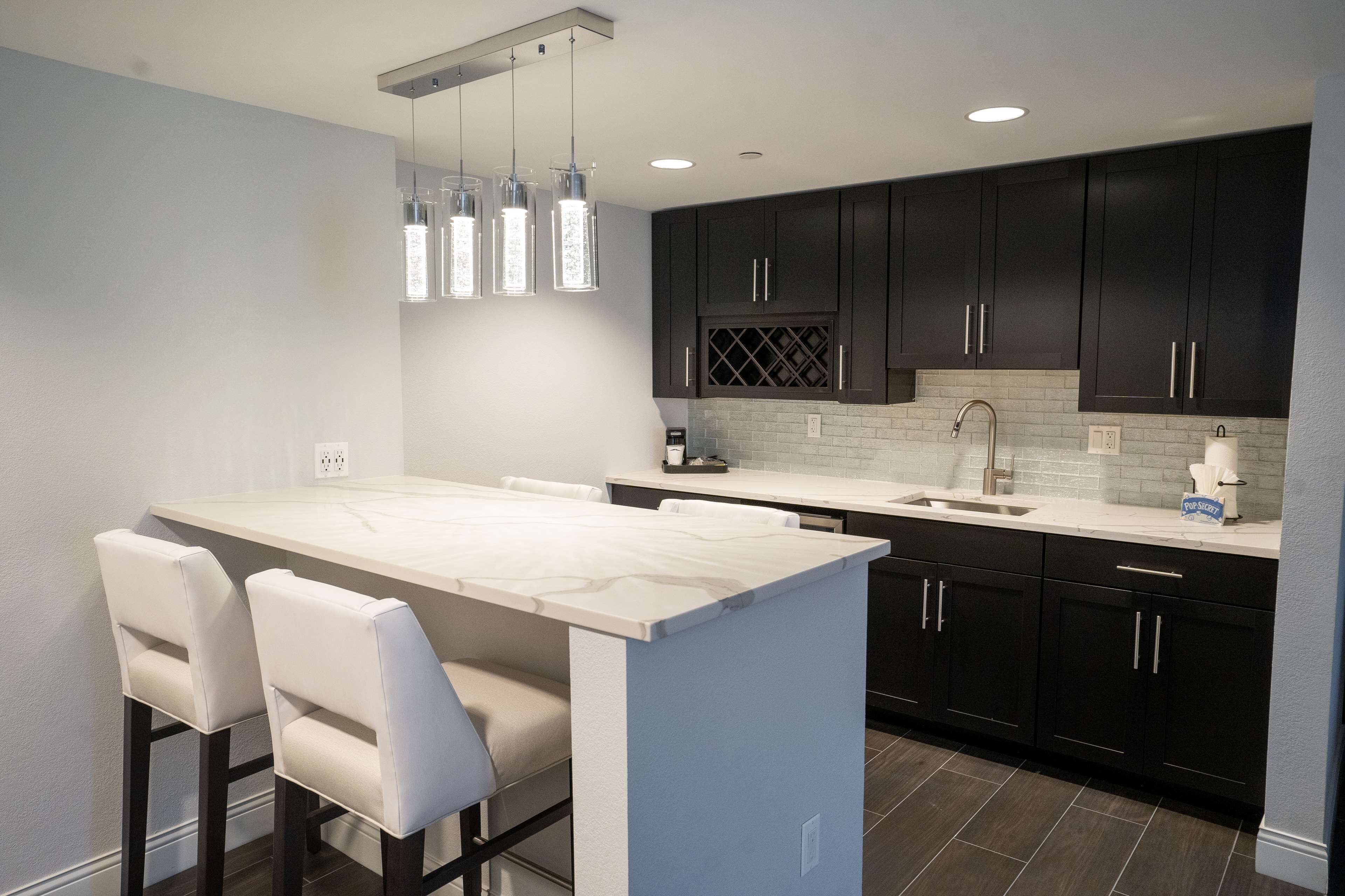 A modern kitchen with dark cabinets, a marble island, and pendant lighting.