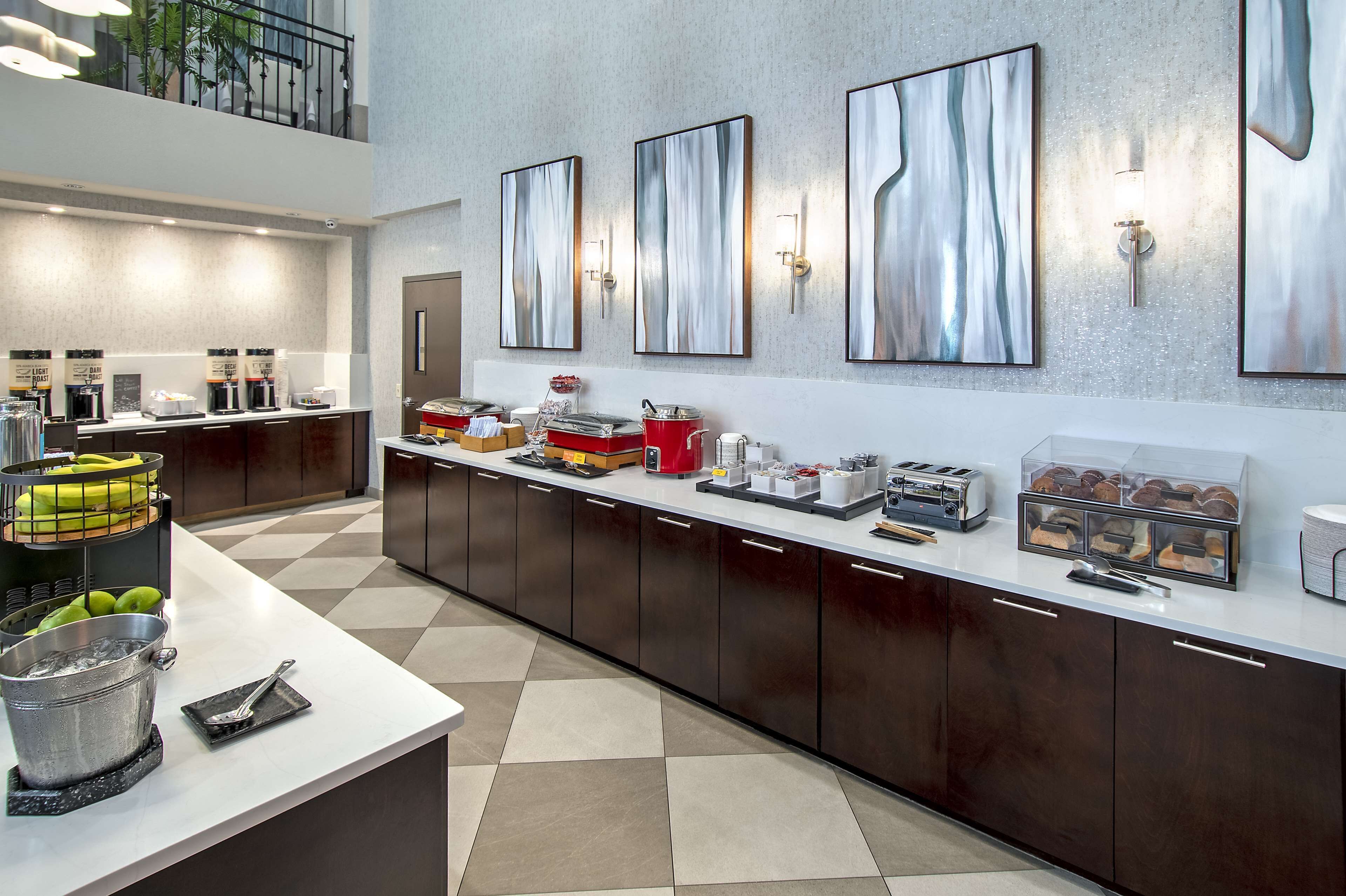 A modern hotel kitchen with a long counter, coffee machines, and a fruit basket.