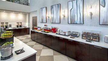 A modern hotel kitchen with a long counter, coffee machines, and a fruit basket.