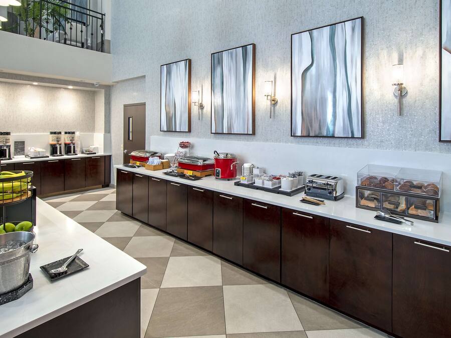 A modern hotel kitchen with a long counter, coffee machines, and a fruit basket.