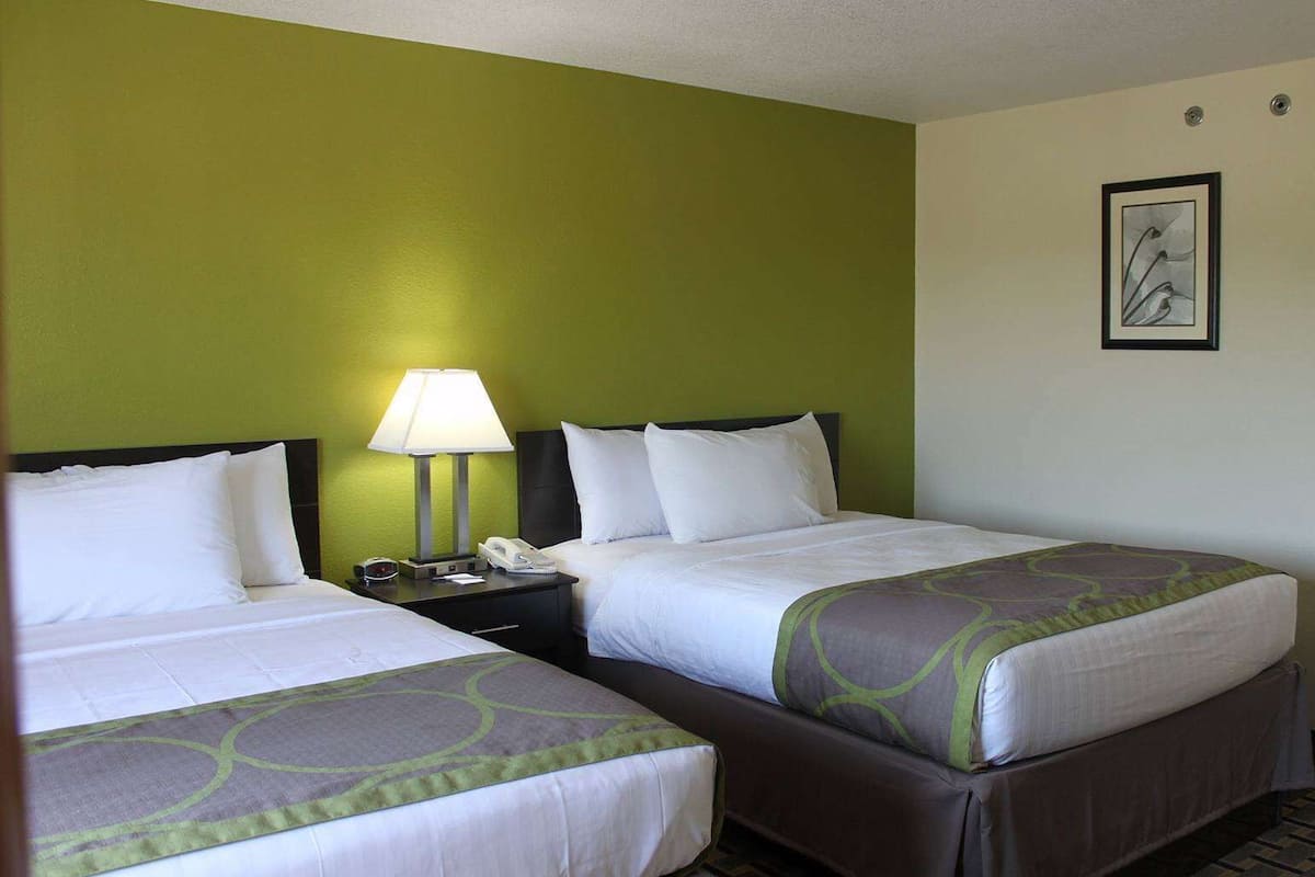 Een hotelkamer met twee bedden, een nachtkastje met een lamp en een lijst aan de muur.