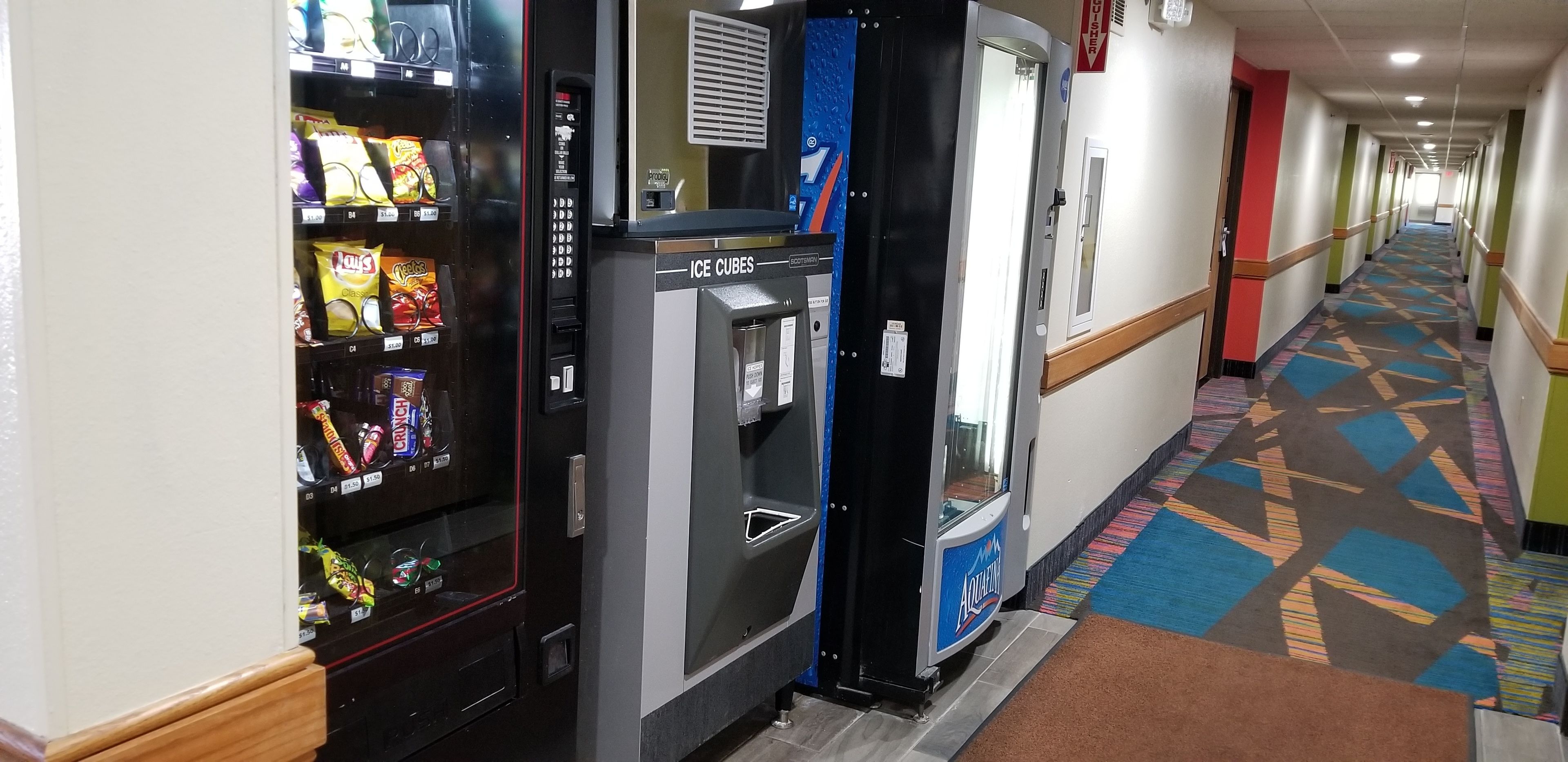 A hotel corridor with vending machines, ice cubes, and a patterned carpet.