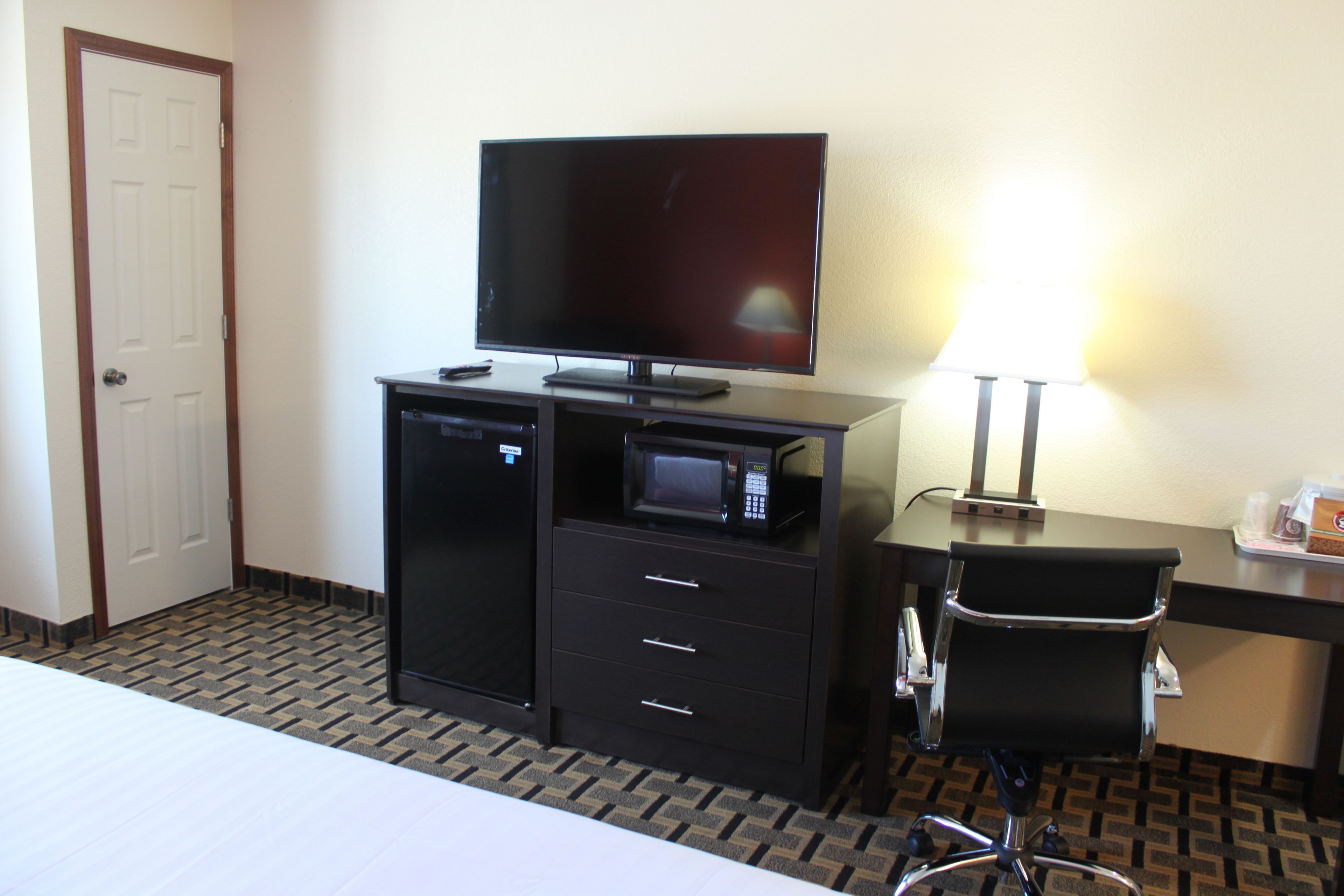 Quarto de hotel com cama, televisão, micro-ondas, escrivaninha e cadeira.