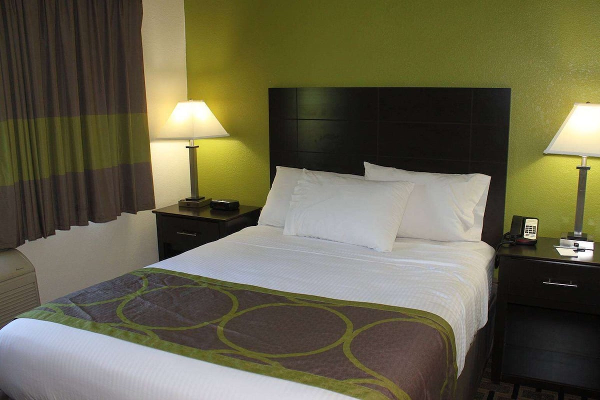 Een hotelkamer met een bed, twee nachtkastjes, een lamp en een telefoon.