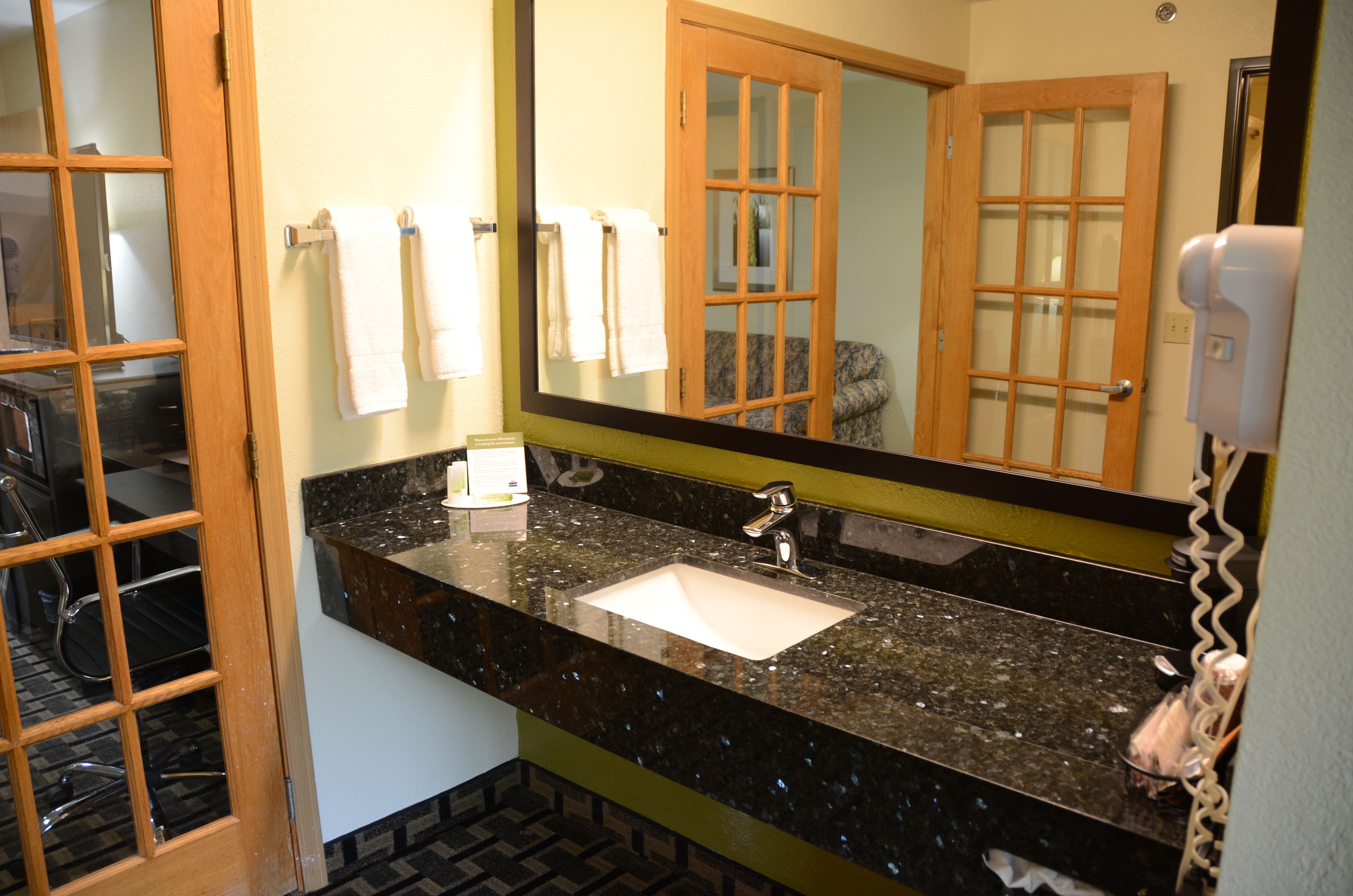 A bathroom with a granite countertop sink, a mirror, and a towel rack.