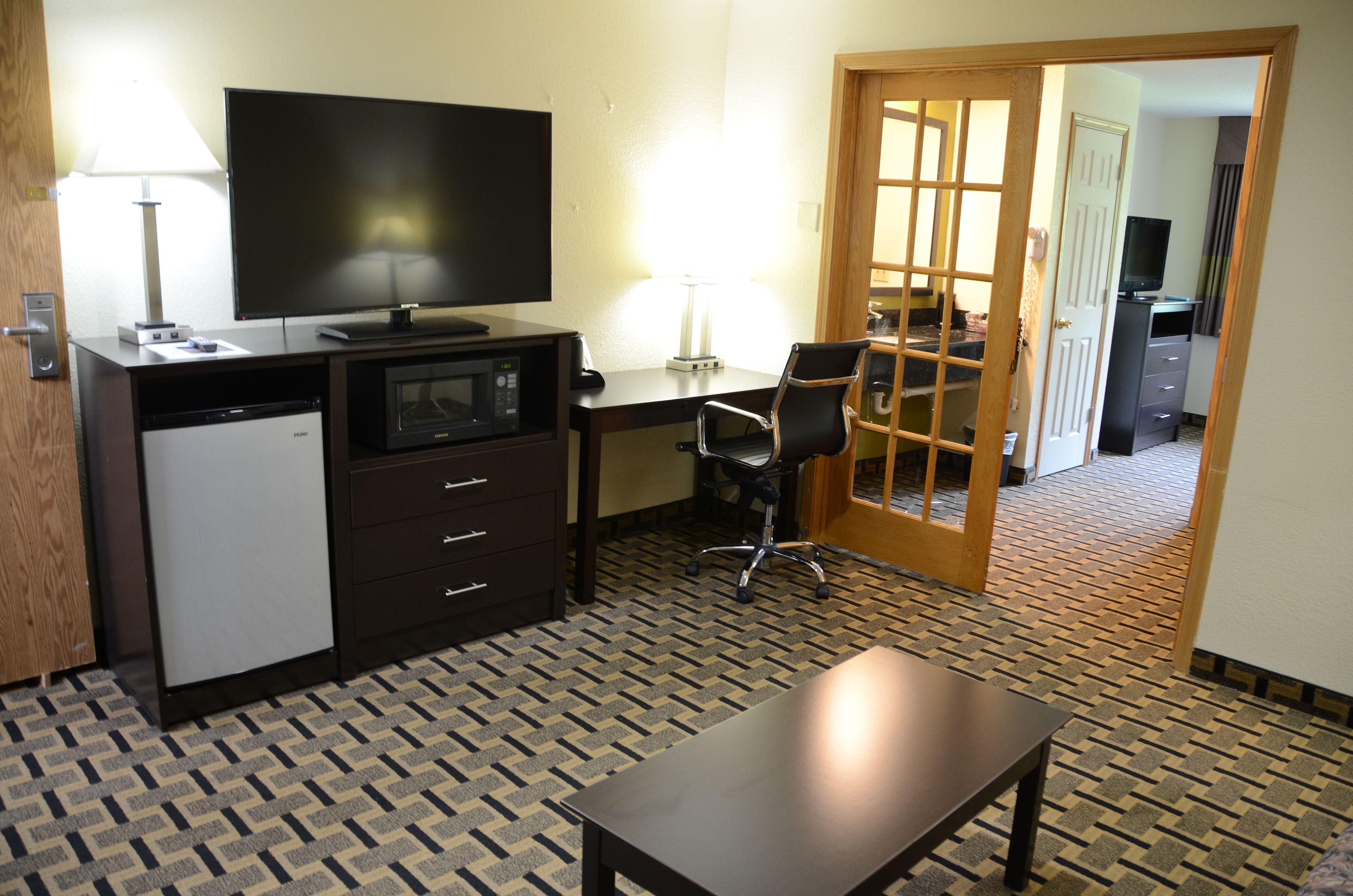 A hotel room with a desk, chair, television, and a microwave.