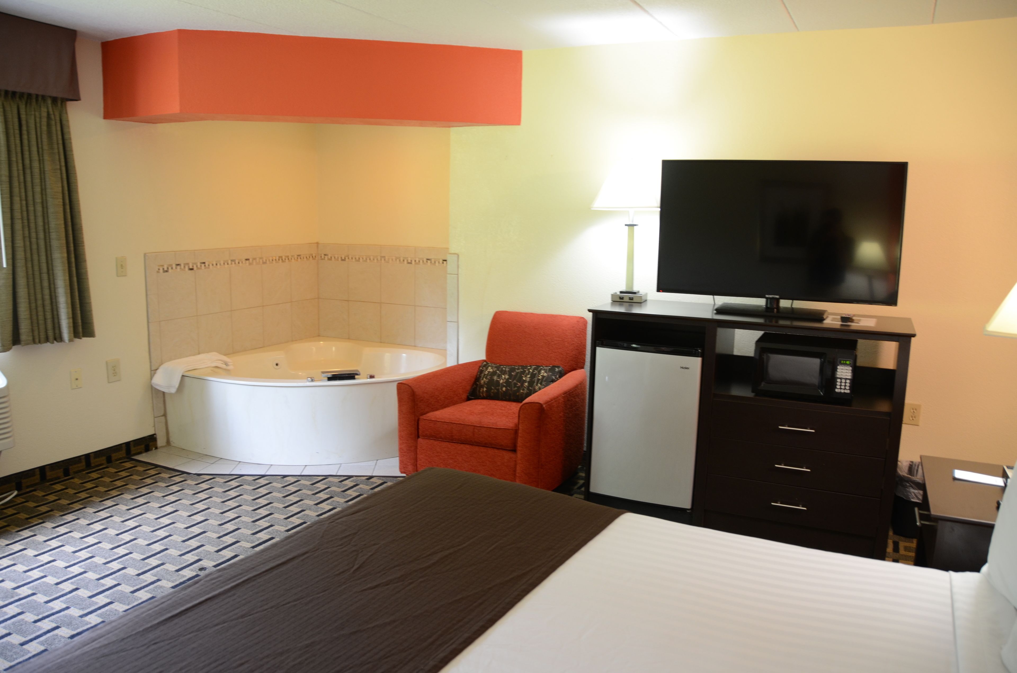Une chambre d’hôtel avec un lit, un fauteuil rouge, un petit bureau avec une télévision, un four à micro-ondes et une baignoire.