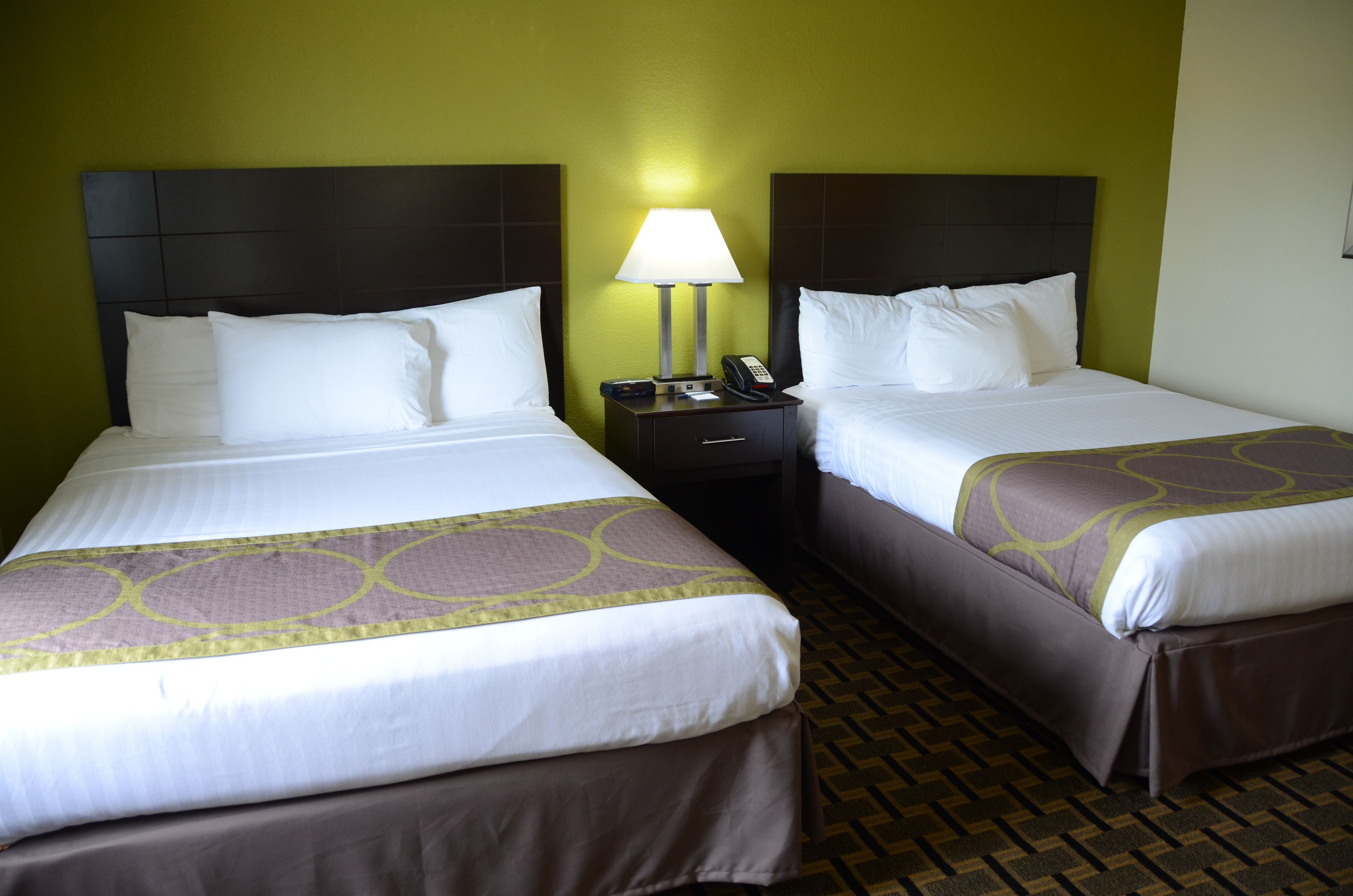 A hotel room with two beds, each with a headboard, a bedside table with a lamp, and a phone.