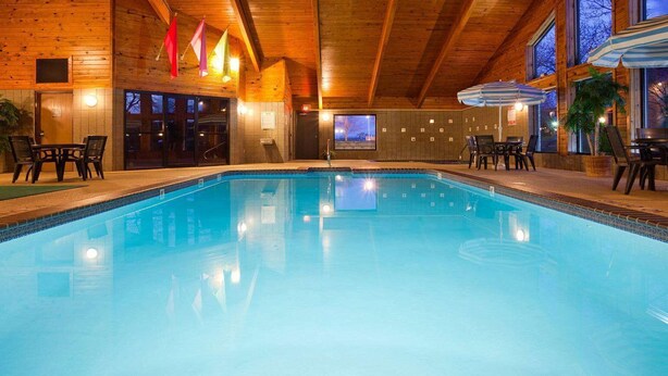 Une piscine intérieure bien éclairée, avec des murs et un plafond en bois, entourée de chaises longues et de parasols.