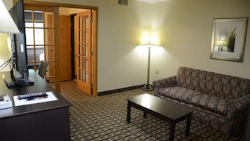 Ein Hotelzimmer mit einem gemusterten Boden, einem Sofa, einem Schreibtisch mit Lampe und einer Tür zu einem anderen Raum.