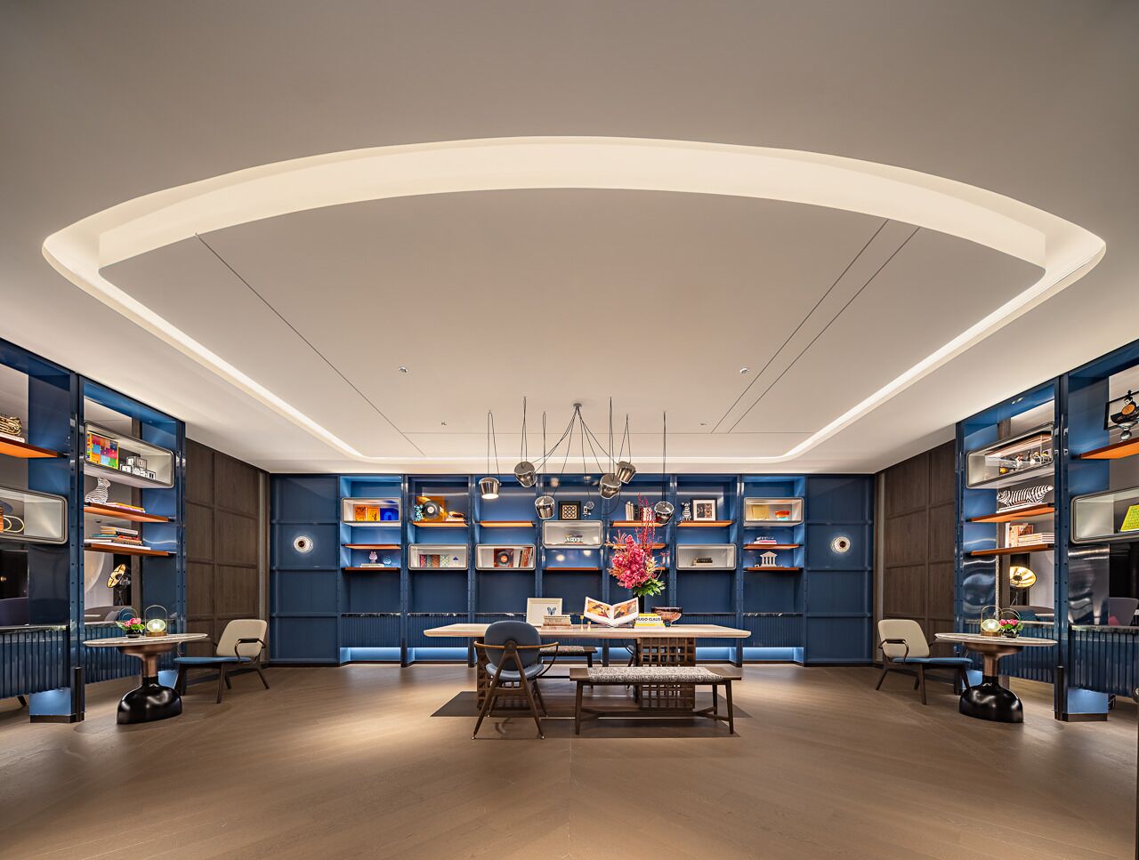 A modern library with bookshelves, a central table, and chairs.