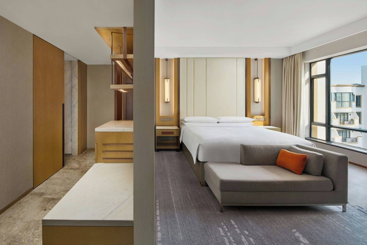 A hotel room with a bed, a sofa, a desk, and a large window.