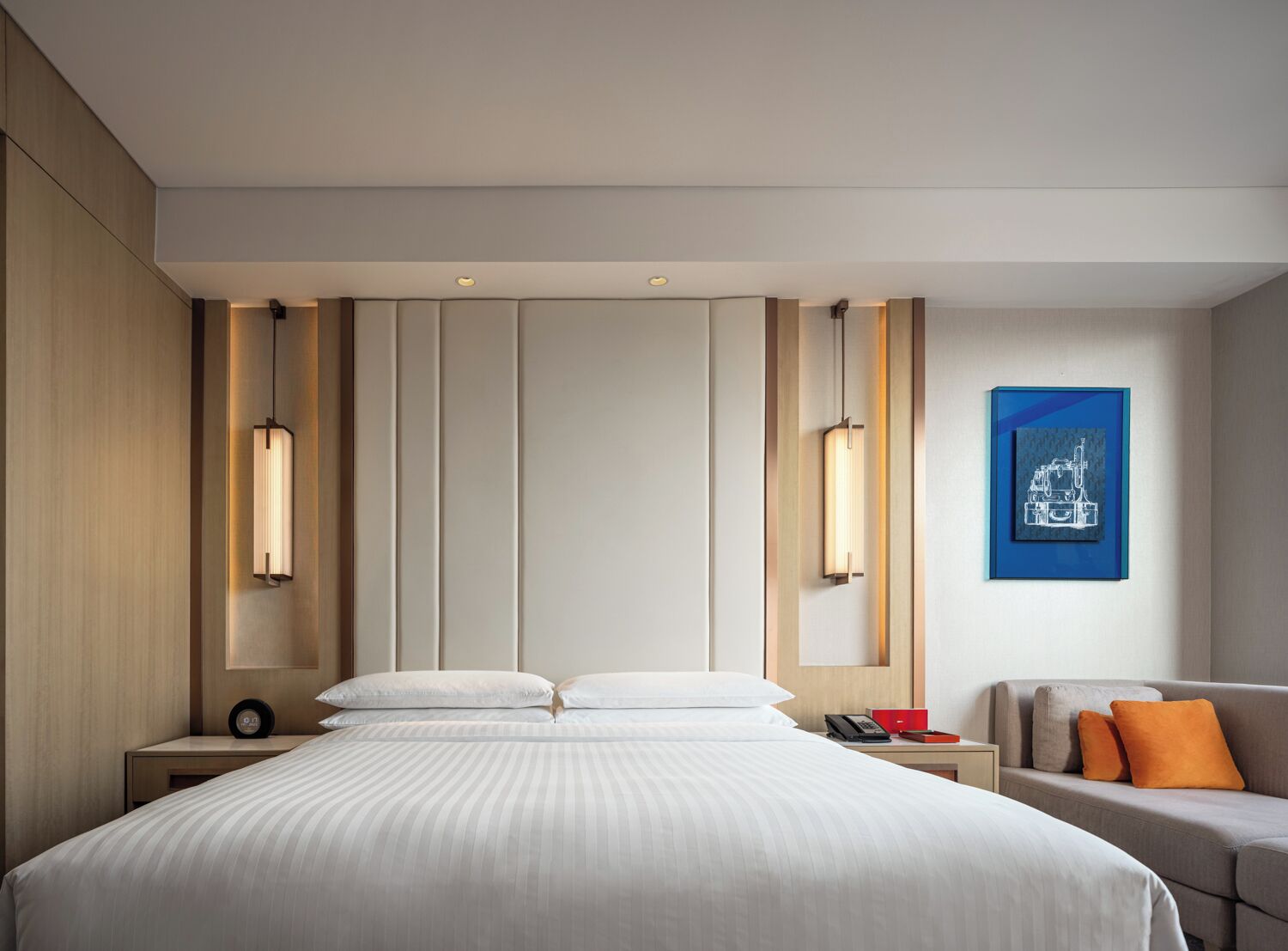 A modern hotel room with a large bed, bedside tables, a desk, and a sofa.