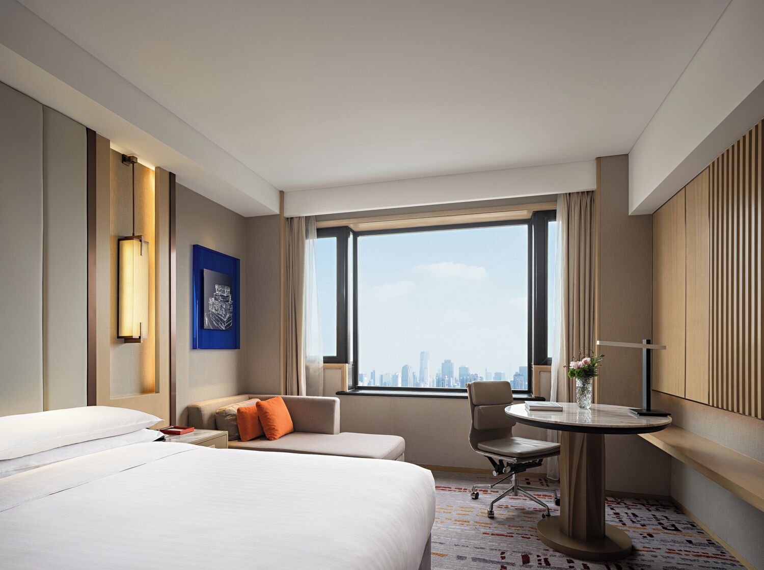 Habitación de hotel con cama, sofá, escritorio y silla. Se ve una ventana con vista a la ciudad.