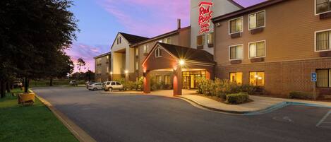 A hotel with a prominent Red Roof Inn sign, a brick facade, and a parking lot with several cars.