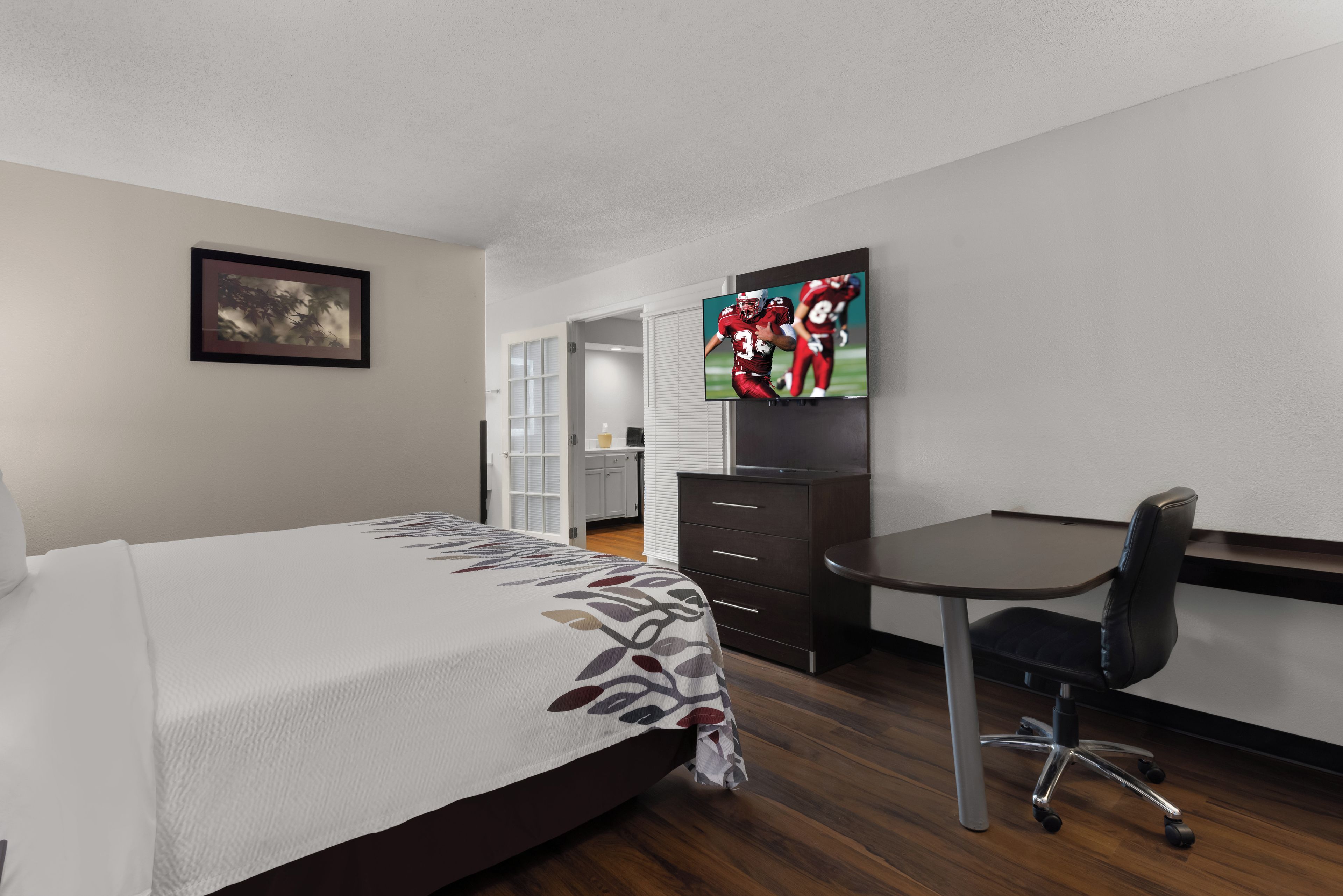 Una habitación de hotel con una cama, un escritorio, una silla, un televisor y un cuadro en la pared.