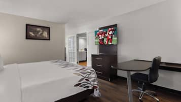 Una habitación de hotel con una cama, un escritorio, una silla, un televisor y un cuadro en la pared.