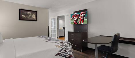 A hotel room with a bed, a desk, a chair, a television, and a framed picture on the wall.