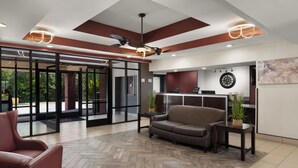 A modern lobby with a herringbone floor, a sofa, a coffee table, and a reception desk with a phone. - Red Roof Inn & Suites Savannah Airport (Pooler)