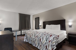 Une chambre d’hôtel équipée d’un lit, d’un bureau, d’une chaise, d’une table de chevet et d’une lampe fixée au mur.