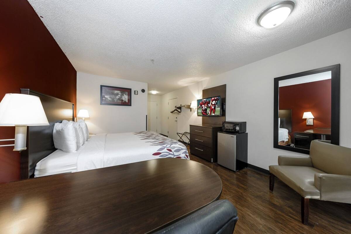 A hotel room with a bed, a desk, a chair, a TV, a microwave, a dresser, and a mirror.