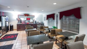 A restaurant with a counter, seating area, and a large window with blinds.