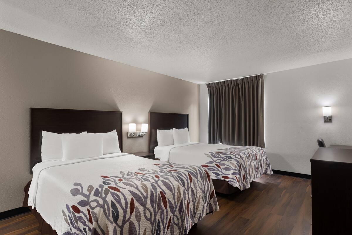 A hotel room with two beds, a desk, and a window with curtains.