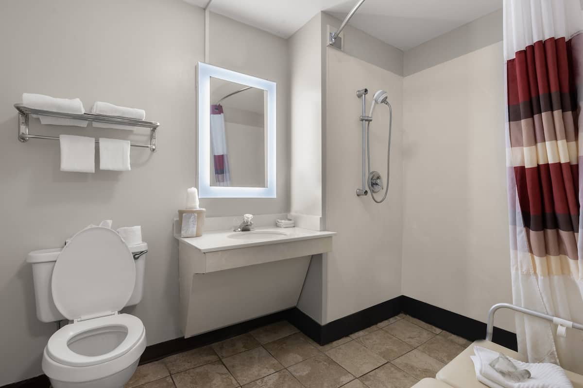 Un baño con inodoro, lavabo, espejo, toallero, ducha y cortina de ducha a rayas.
