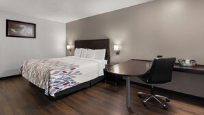 A hotel room with a bed, bedside table, chair, and a desk with a chair. - Red Roof Inn & Suites Savannah Airport (Pooler)