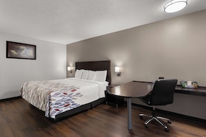 A hotel room with a bed, bedside table, chair, and a desk with a chair. - Red Roof Inn & Suites Savannah Airport (Pooler)