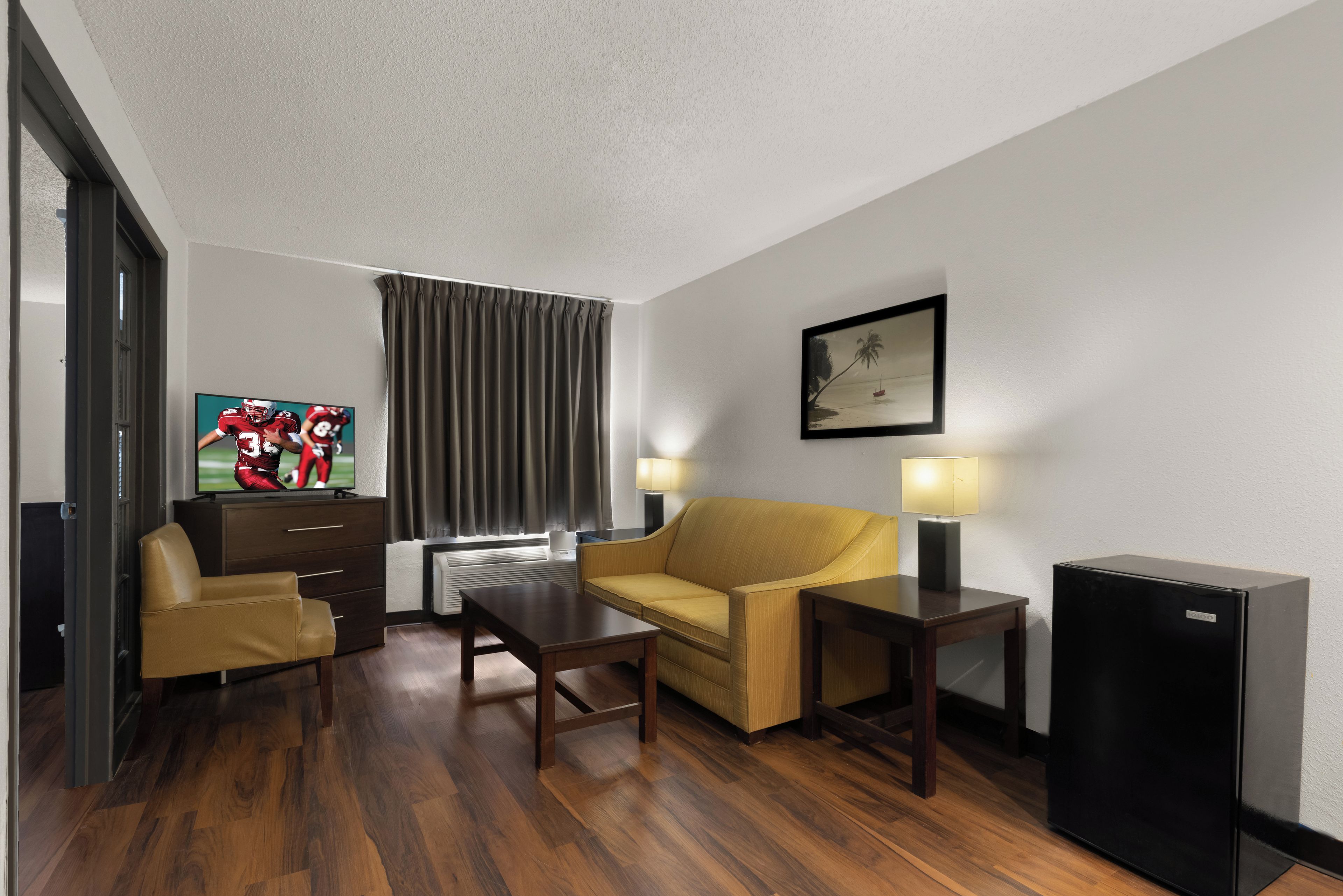 Una habitación de hotel con sofá, una mesita, televisión, lámpara y refrigerador.
