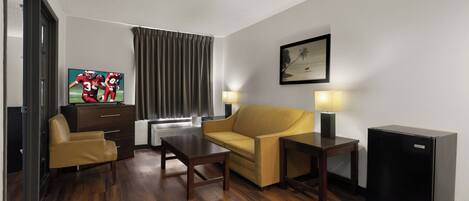 A hotel room with a sofa, a small table, a TV, a lamp, and a refrigerator.