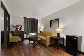 Een hotelkamer met een bank, een klein tafeltje, een televisie, een lamp en een koelkast.