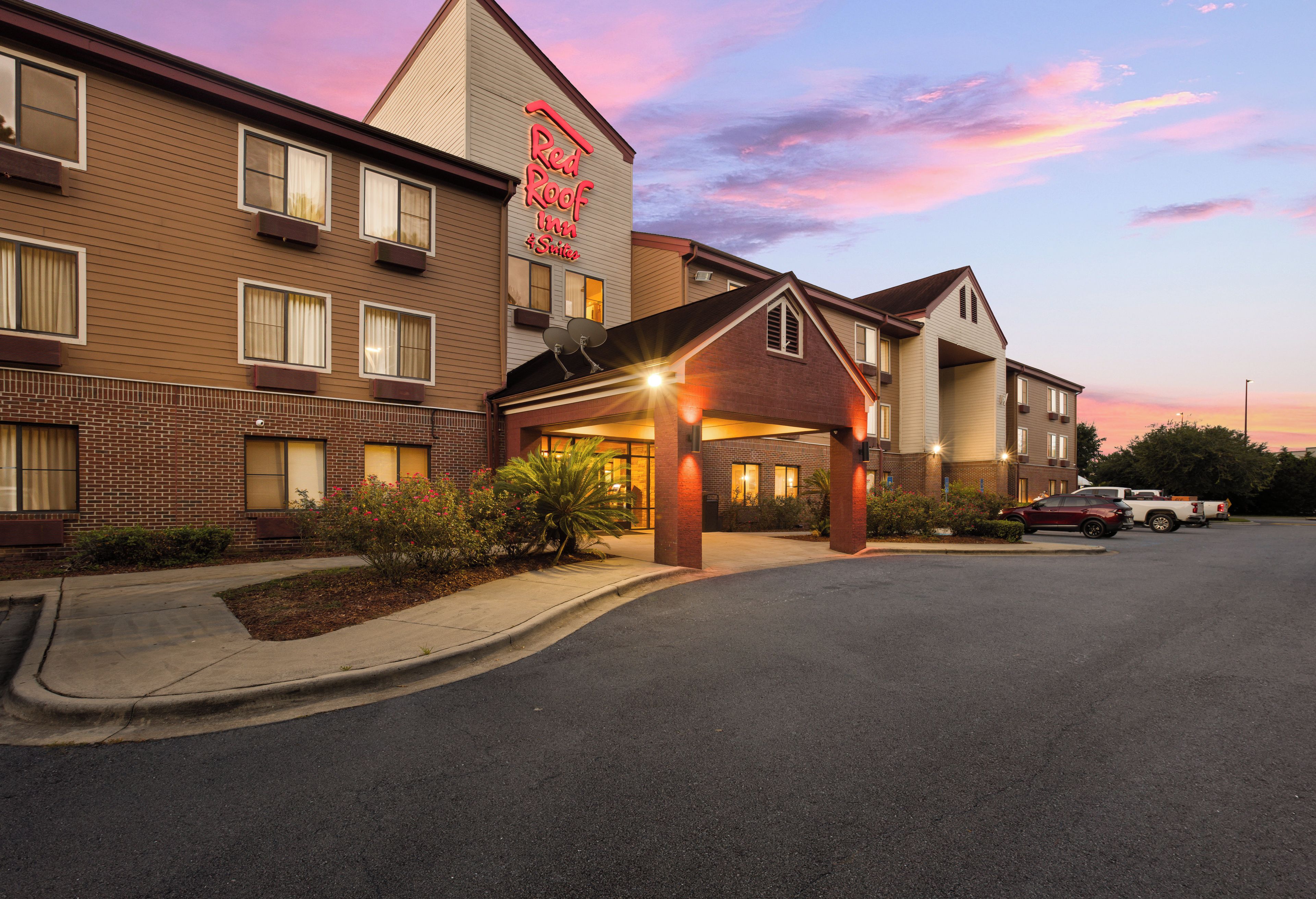 A hotel with a prominent red sign, a covered entrance, and a parking lot.