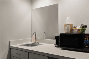 A modern bathroom with a sink, mirror, and a coffee machine. - Red Roof Inn & Suites Savannah Airport (Pooler)