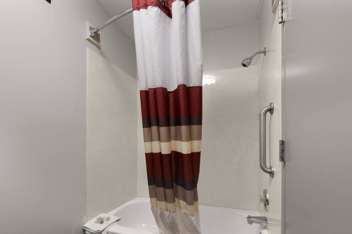 Una ducha con cortina a rayas, cabezal de ducha de mano y grifo empotrado en la pared.