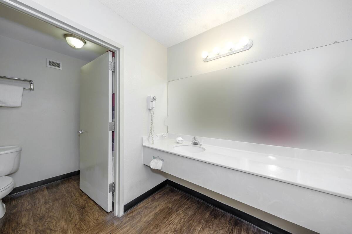 A bathroom with a toilet, a sink with a mirror, and a hairdryer on the wall.