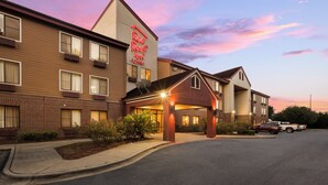 A hotel with a prominent red sign, a covered entrance, and a parking lot with cars.