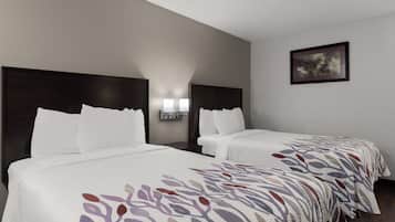 Una habitación de hotel con dos camas, cada una con ropa de cama blanca y una manta estampada. Hay luces fijadas en la pared sobre las camas y un cuadro enmarcado en la pared.