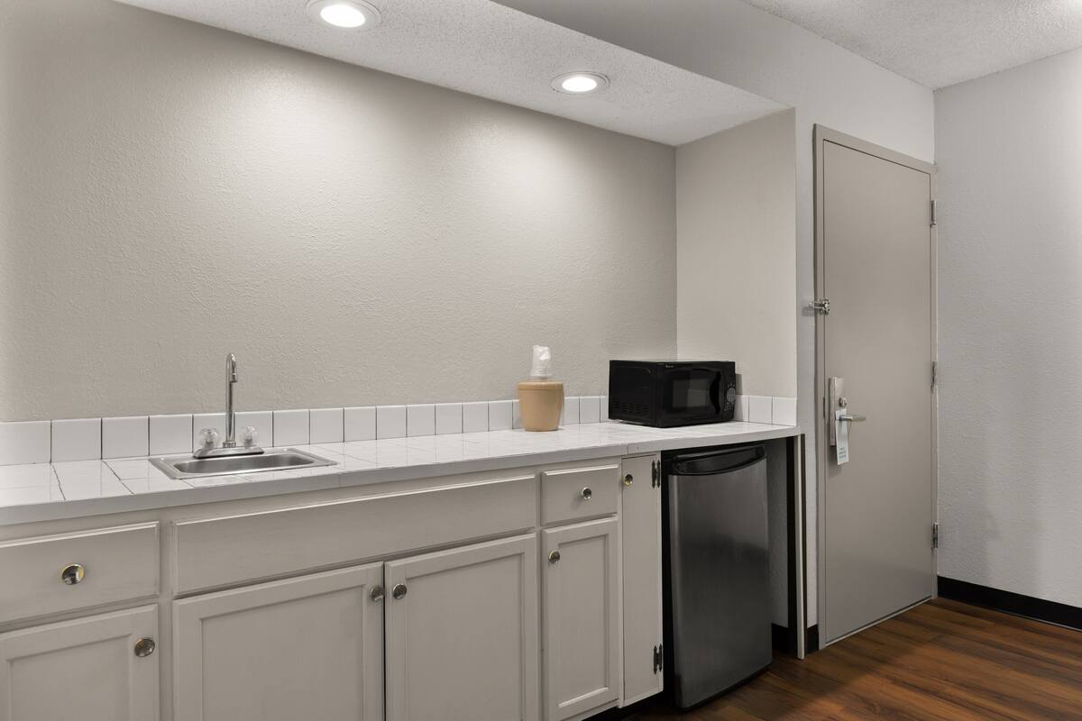 A compact kitchen with white cabinets, a stainless steel sink, a microwave, and a dishwasher.