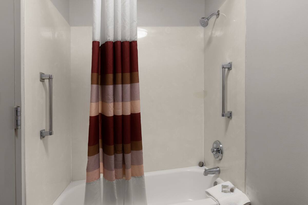 Ducha con cortina a rayas, una bañera blanca y un cabezal de ducha de mano.